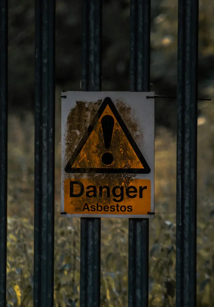 An asbestos danger warning sign attached via zip ties to a black fence.