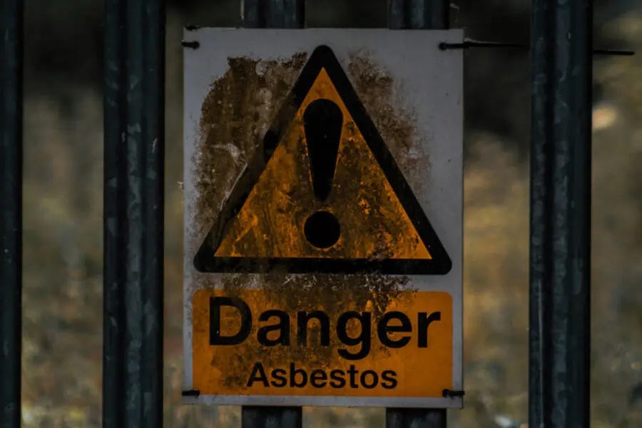 An asbestos danger warning sign attached via zip ties to a black fence.